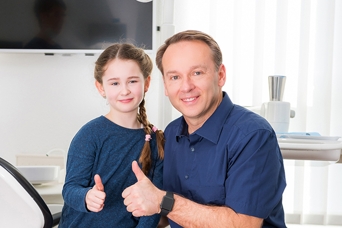 Dr. Kowallik und ein Mädchen zeigen Daumen nach oben - Dymbolbild für Kinderzahnmedizin