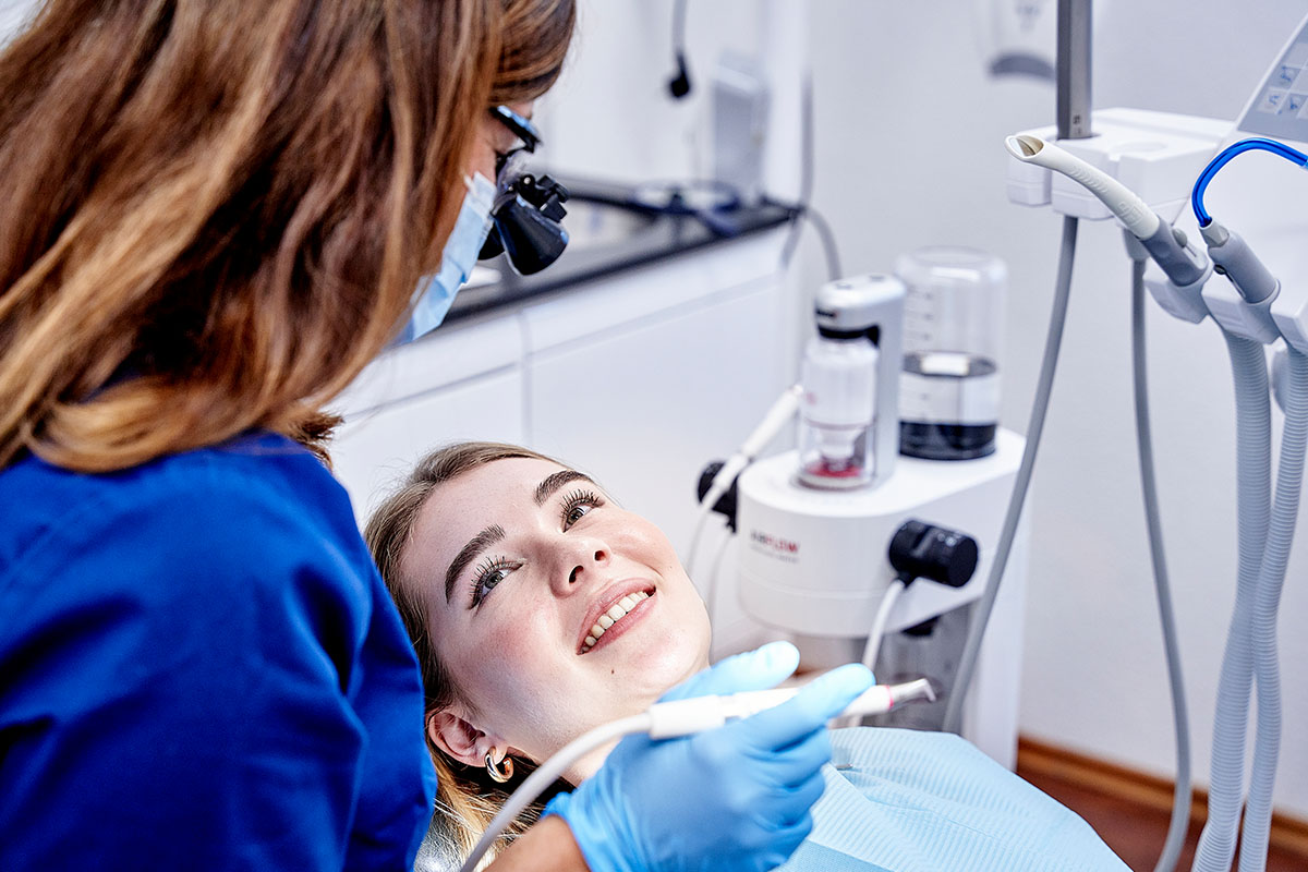 Parodontitisbehandlung in der Zahnarztpraxis Kowadent Hückelhoven: Zahnärztin beugt sich über die Patientin und untersucht die Zähne.