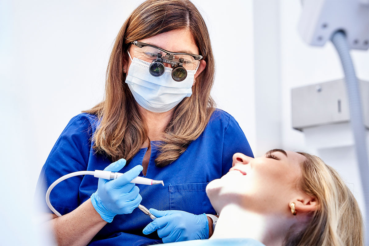Zahnärztin mit Lupenbrille über Patientin auf dem Stuhl – Symbolbild für Feste Zähne an einem Tag